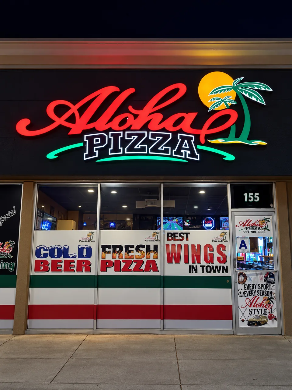 Aloha Pizza illuminated logo above printed storefront window graphics